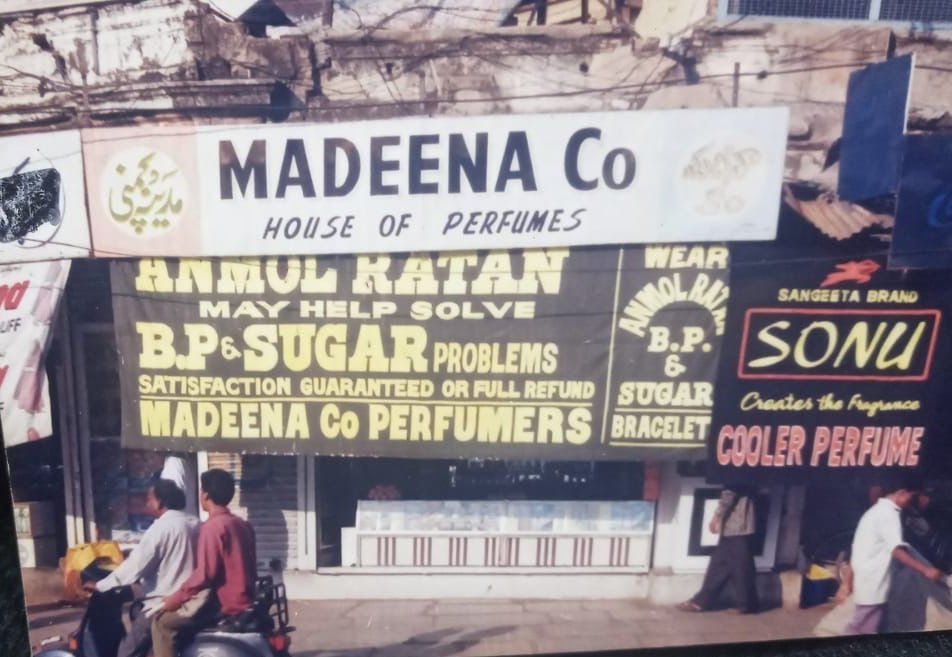 Vintage advertisement poster for Madeena Co Perfumes featuring people and buildings.